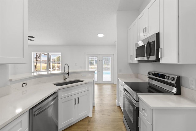 kitchen with sink, ceiling fan, light wood-type flooring, white cabinetry, and stainless steel appliances