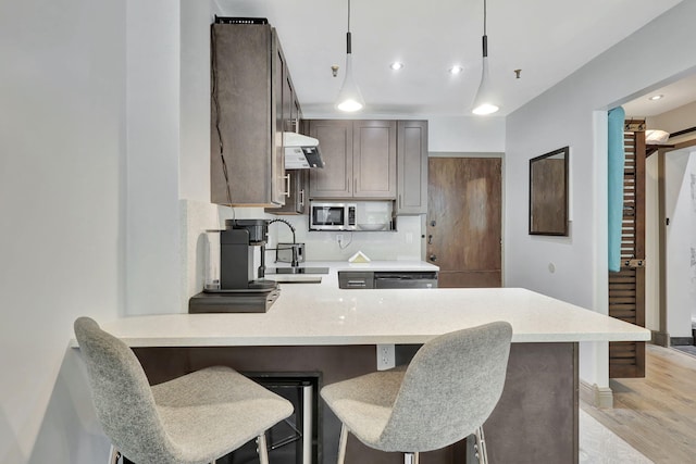 kitchen with kitchen peninsula, backsplash, a breakfast bar, sink, and decorative light fixtures