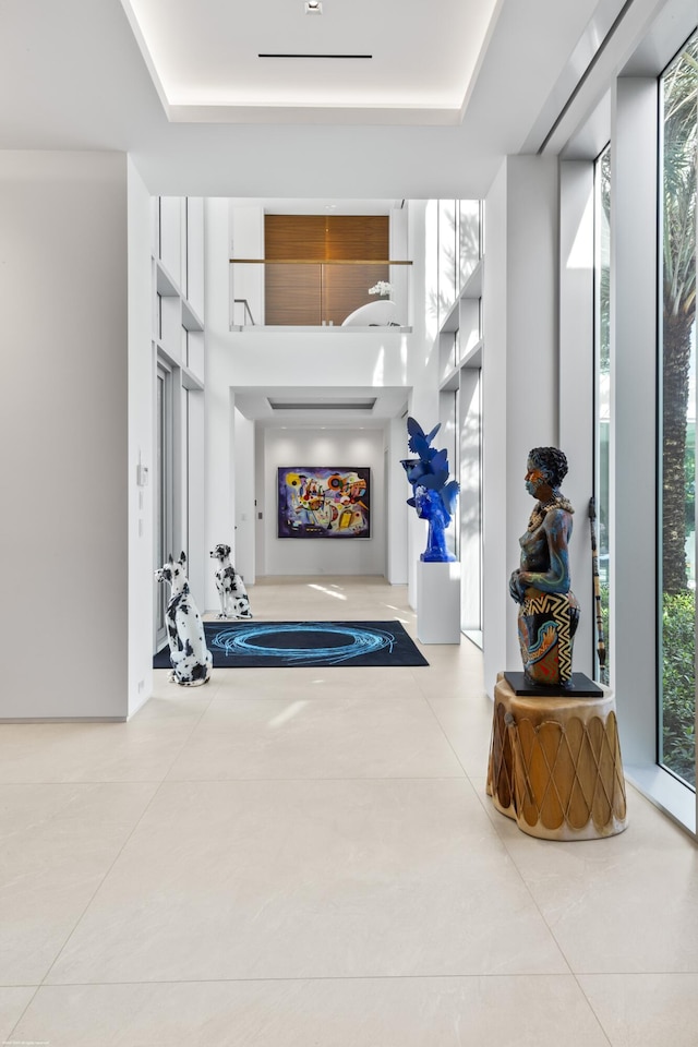 corridor featuring plenty of natural light, a raised ceiling, and light tile patterned floors