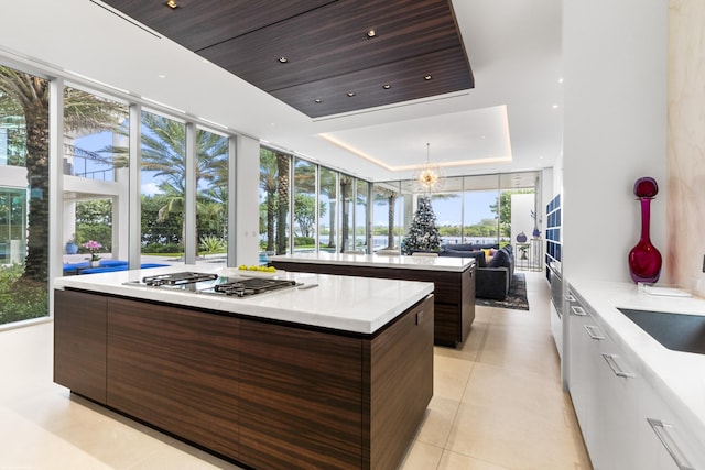 kitchen featuring a tray ceiling, stainless steel gas cooktop, light tile patterned floors, a center island, and white cabinetry