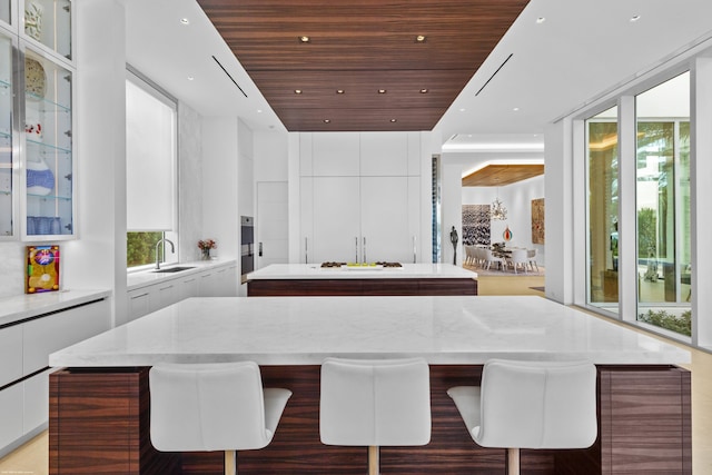 interior space featuring sink, white cabinetry, a kitchen island, wood ceiling, and a breakfast bar area