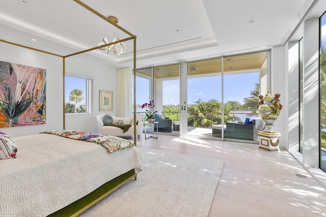 bedroom featuring access to outside, floor to ceiling windows, a tray ceiling, and an inviting chandelier