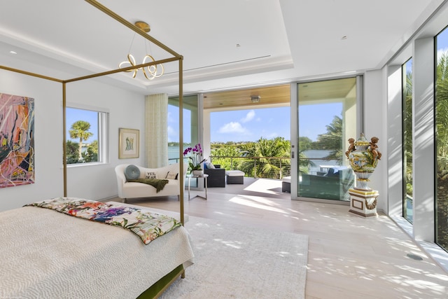 bedroom featuring a chandelier, access to outside, a tray ceiling, and a wall of windows