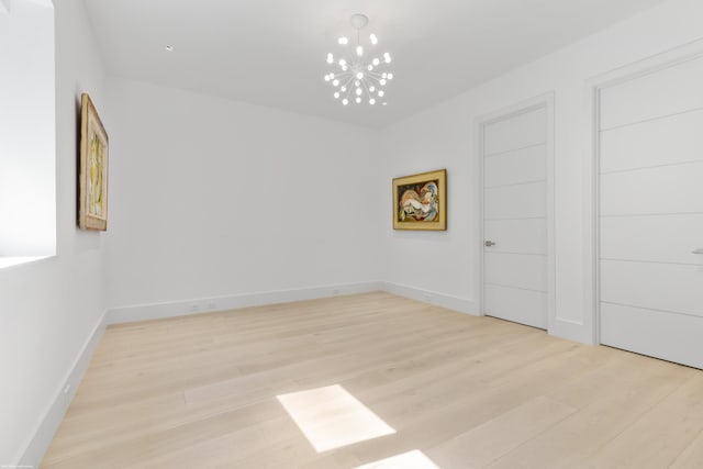 empty room with an inviting chandelier and light hardwood / wood-style flooring