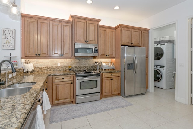 kitchen featuring light stone countertops, appliances with stainless steel finishes, decorative backsplash, sink, and stacked washer / drying machine