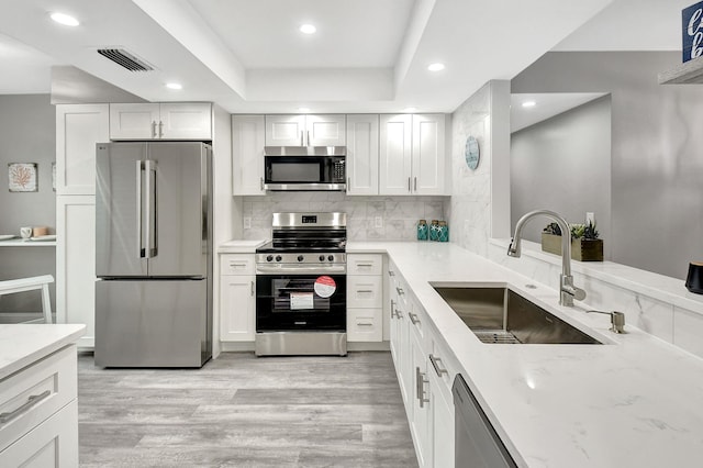 kitchen featuring a raised ceiling, sink, white cabinets, and appliances with stainless steel finishes