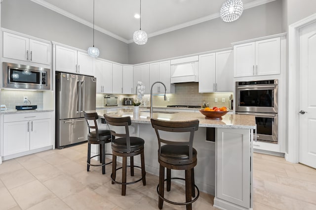 kitchen with premium range hood, a center island with sink, hanging light fixtures, appliances with stainless steel finishes, and white cabinetry