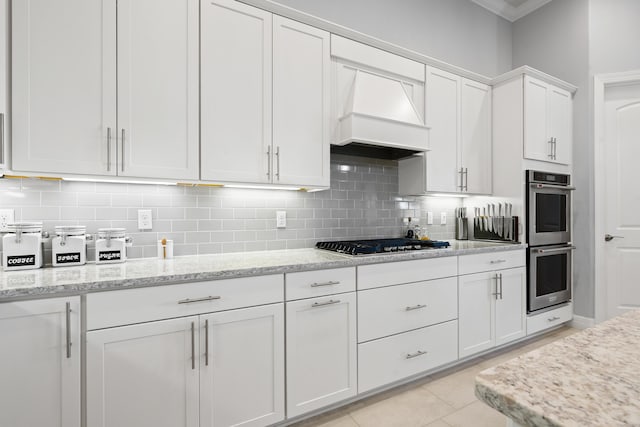 kitchen with appliances with stainless steel finishes, backsplash, light stone counters, custom exhaust hood, and white cabinets