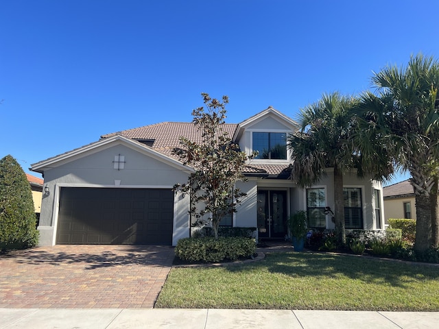 view of front of property featuring a garage, a tile roof, decorative driveway, stucco siding, and a front yard