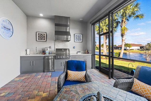 bar featuring gray cabinetry, sink, wall chimney range hood, decorative backsplash, and a water view