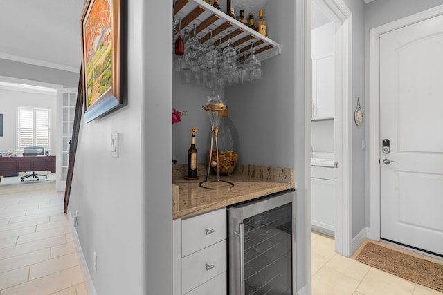 bar with white cabinets, light stone countertops, light tile patterned floors, ornamental molding, and beverage cooler