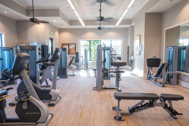 workout area featuring light wood finished floors, baseboards, a tray ceiling, and ornamental molding