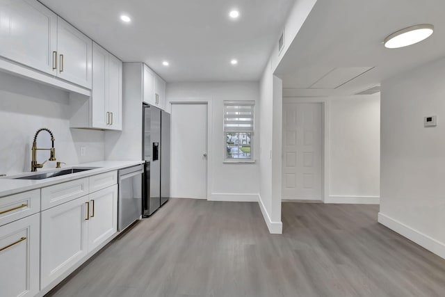 kitchen with stainless steel appliances, light countertops, white cabinets, a sink, and light wood-type flooring