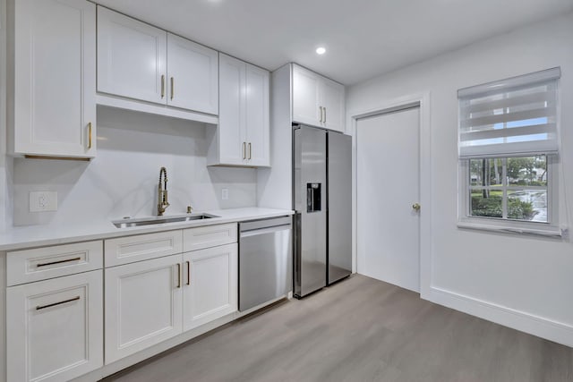 kitchen featuring stainless steel appliances, a sink, white cabinetry, light wood-style floors, and light countertops