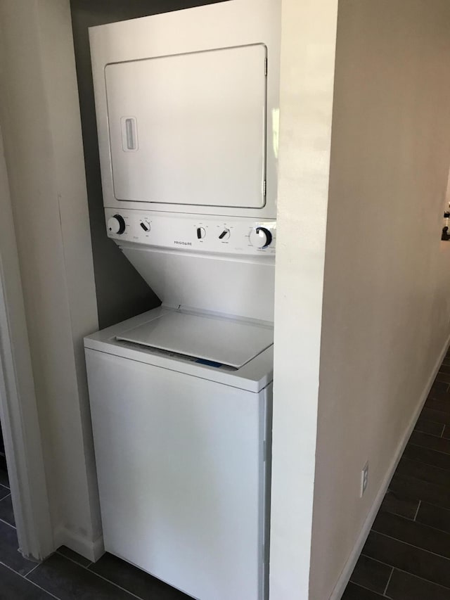 laundry area with dark tile patterned floors and stacked washer / drying machine