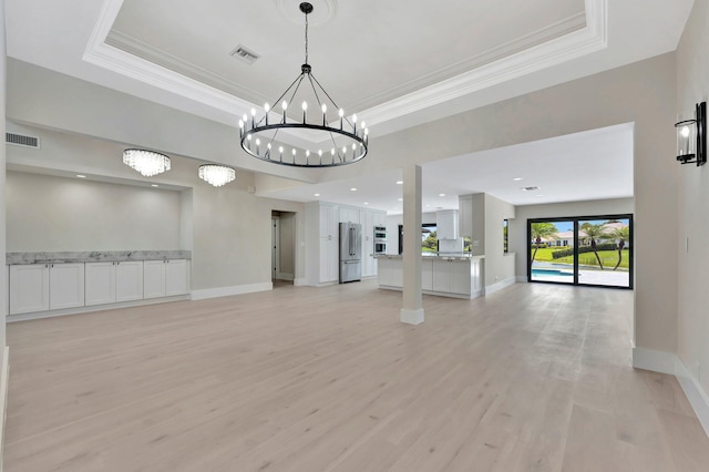 spare room with a raised ceiling, a notable chandelier, crown molding, and light hardwood / wood-style flooring