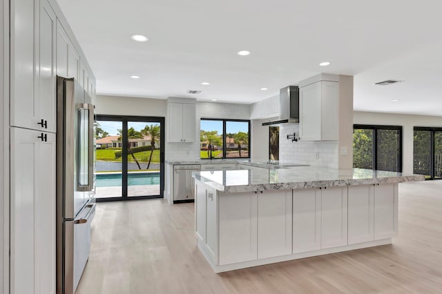 kitchen with white cabinets, appliances with stainless steel finishes, wall chimney exhaust hood, decorative backsplash, and kitchen peninsula