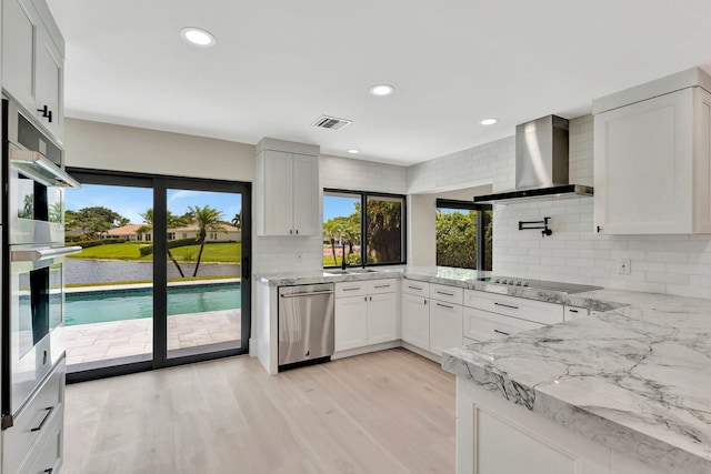 kitchen with white cabinets, backsplash, appliances with stainless steel finishes, and wall chimney exhaust hood