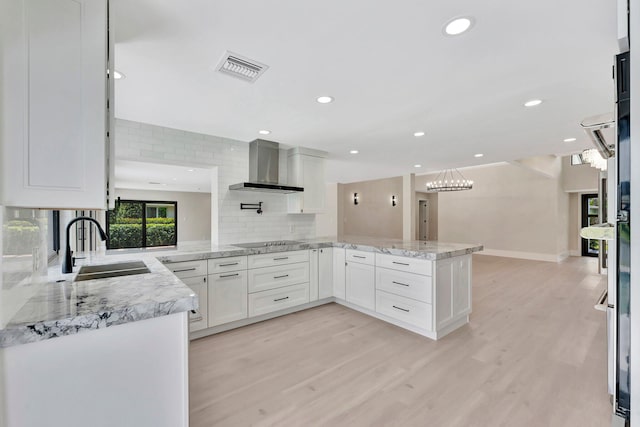 kitchen featuring light wood-type flooring, white cabinetry, kitchen peninsula, and wall chimney range hood