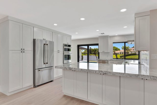 kitchen featuring light stone countertops, kitchen peninsula, white cabinets, and stainless steel appliances