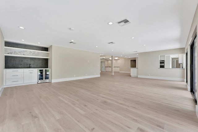 unfurnished living room with wet bar, beverage cooler, and light hardwood / wood-style flooring