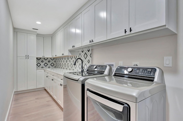 laundry area featuring cabinets, light hardwood / wood-style flooring, and washing machine and clothes dryer