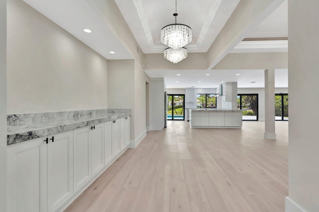 hall with light wood-type flooring, a notable chandelier, a tray ceiling, and ornamental molding