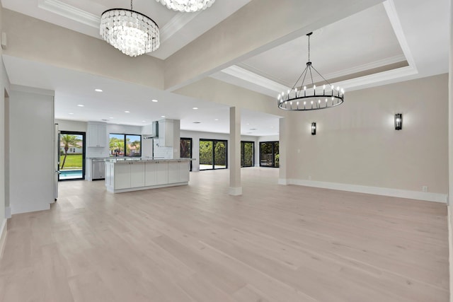 unfurnished living room featuring ornamental molding, a tray ceiling, a chandelier, and light hardwood / wood-style floors