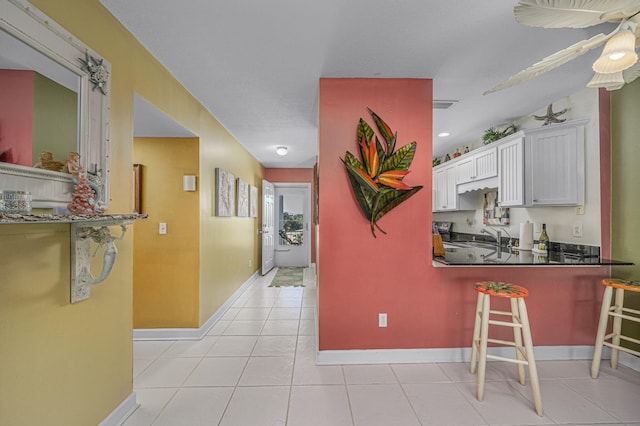 kitchen featuring kitchen peninsula, light tile patterned flooring, white cabinetry, a kitchen breakfast bar, and a textured ceiling