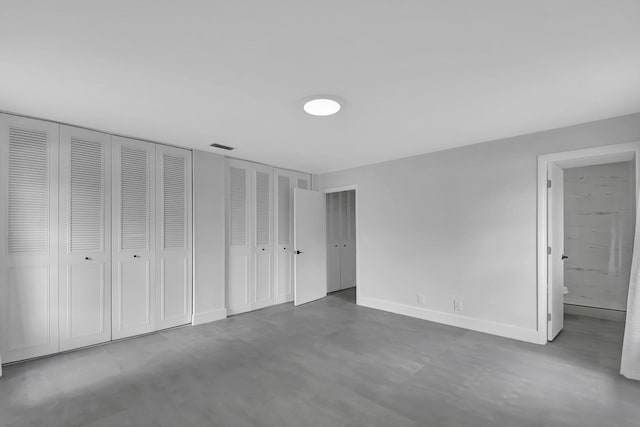 unfurnished bedroom featuring two closets, concrete flooring, and ensuite bath