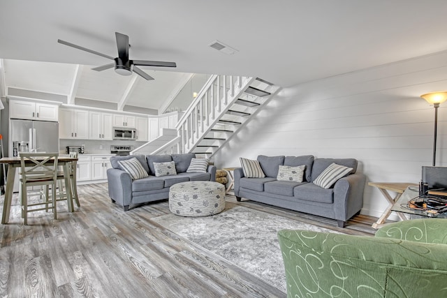 living room featuring light wood-type flooring, ceiling fan, lofted ceiling with beams, and stairs