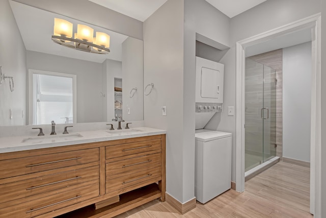 bathroom featuring a shower with door, vanity, stacked washing maching and dryer, and hardwood / wood-style flooring