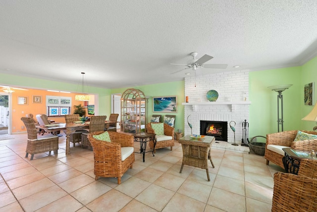 living room with ceiling fan, a brick fireplace, crown molding, a textured ceiling, and light tile patterned floors