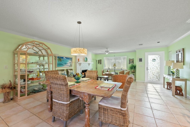 tiled dining area with a textured ceiling, a brick fireplace, ceiling fan, and crown molding