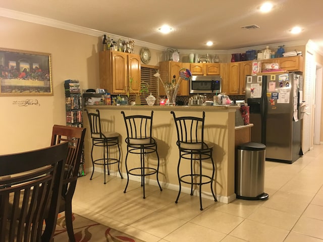 kitchen with kitchen peninsula, ornamental molding, a breakfast bar, stainless steel appliances, and light tile patterned floors