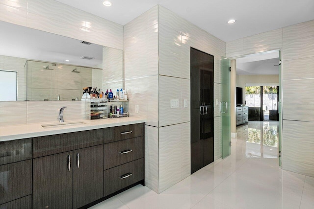 interior space with tile patterned floors, vanity, a shower with shower door, and tile walls