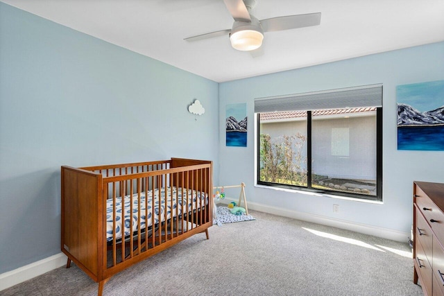 carpeted bedroom with ceiling fan and a nursery area