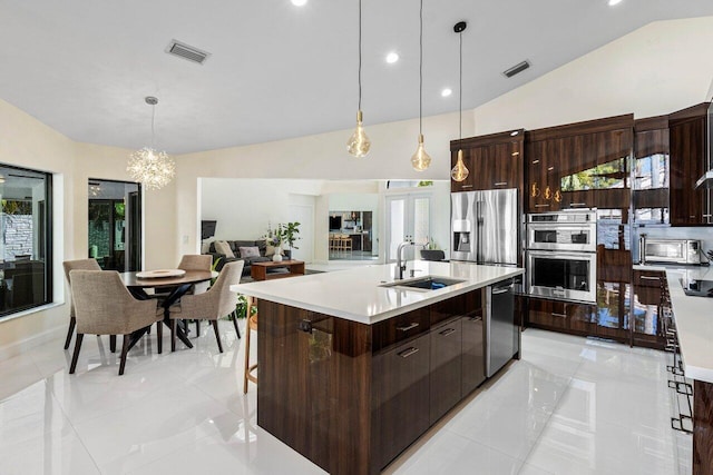 kitchen featuring lofted ceiling, a kitchen island with sink, sink, appliances with stainless steel finishes, and decorative light fixtures