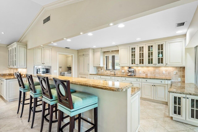 kitchen with stainless steel microwave, decorative backsplash, ornamental molding, a kitchen island, and a breakfast bar area