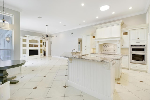 kitchen with a large island with sink, hanging light fixtures, ceiling fan, light tile patterned floors, and stainless steel double oven