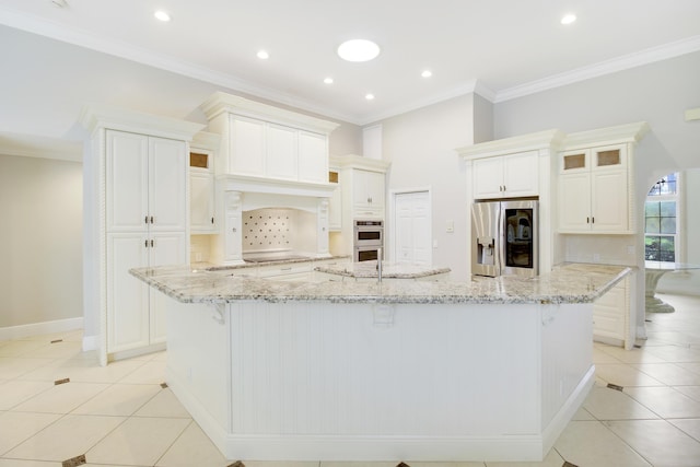 kitchen featuring white cabinets, light stone counters, a large island with sink, and appliances with stainless steel finishes