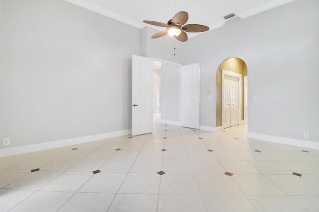 empty room with a high ceiling, ceiling fan, ornamental molding, and light tile patterned flooring