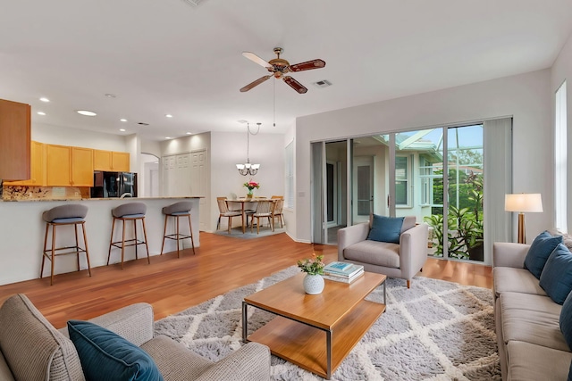 living room with ceiling fan with notable chandelier and light wood-type flooring