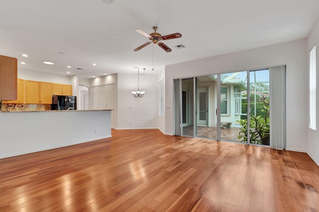 unfurnished living room featuring ceiling fan with notable chandelier and light hardwood / wood-style floors