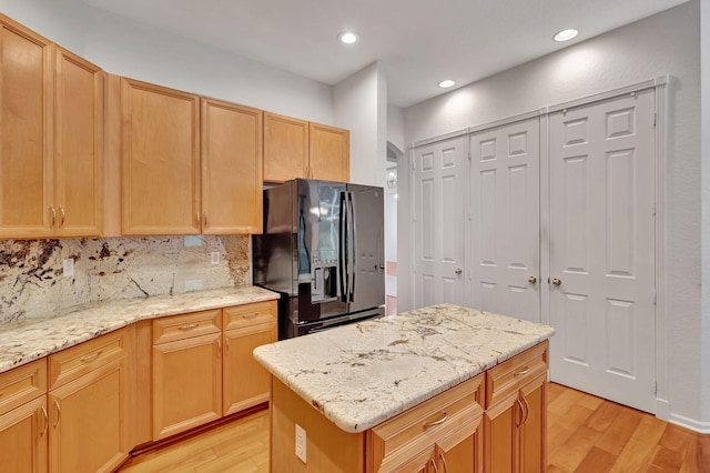 kitchen featuring light stone countertops, backsplash, black fridge, light brown cabinets, and light hardwood / wood-style flooring