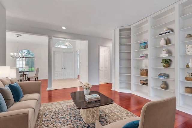 living room featuring a notable chandelier, wood-type flooring, built in features, and ornate columns