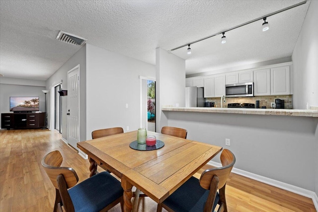 dining room featuring rail lighting, light wood-type flooring, and a textured ceiling