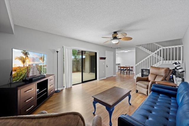 living room with ceiling fan, light wood-type flooring, and a textured ceiling