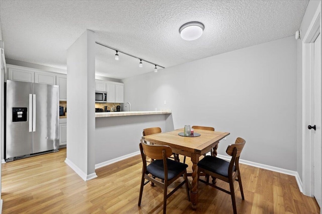 dining room with a textured ceiling, rail lighting, and light hardwood / wood-style flooring