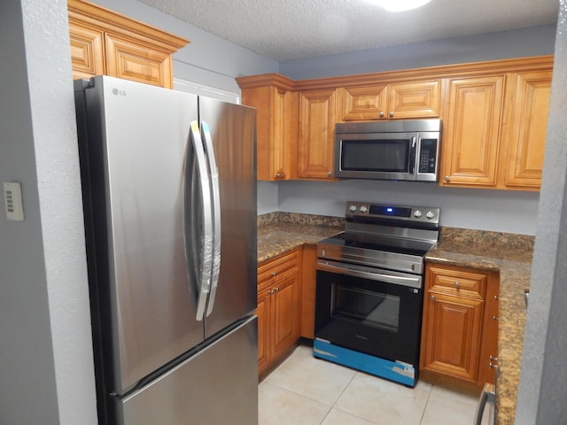 kitchen featuring light tile patterned flooring, stainless steel appliances, a textured ceiling, and dark stone countertops